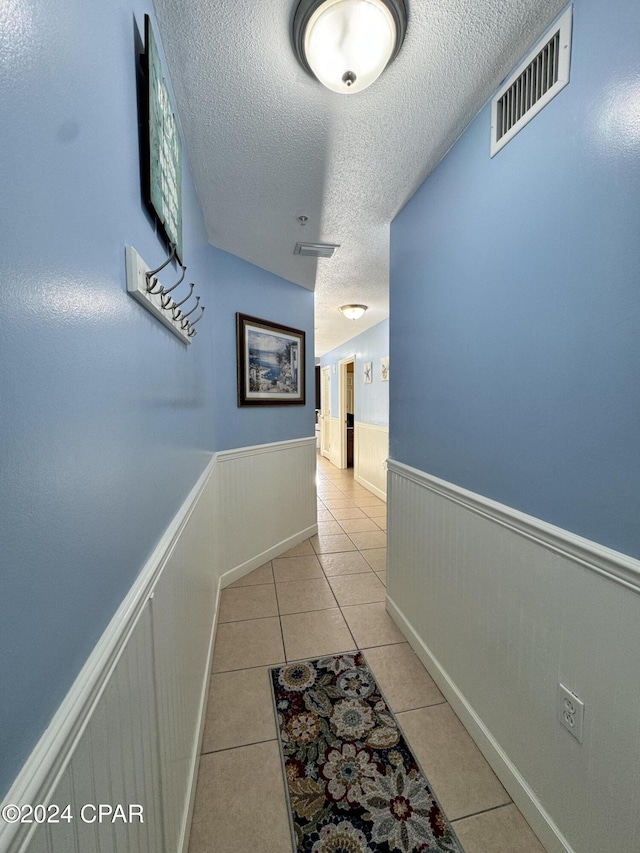 hall featuring light tile patterned floors and a textured ceiling