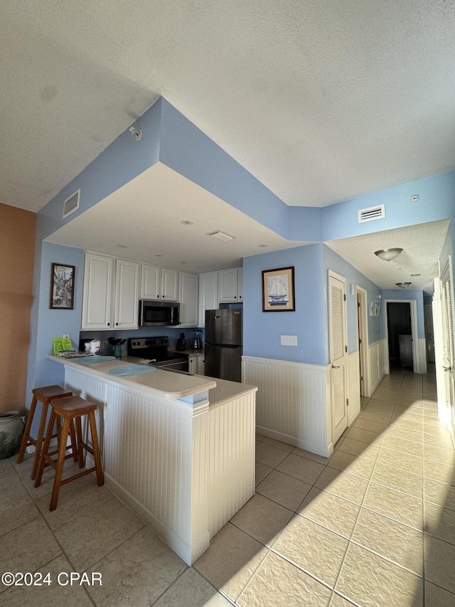 kitchen featuring kitchen peninsula, black range with electric cooktop, white cabinetry, and fridge