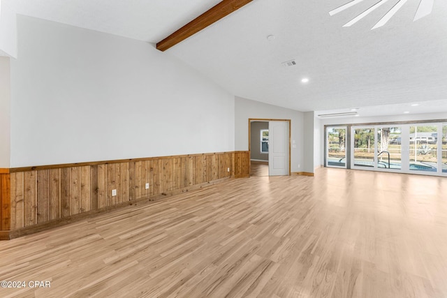 unfurnished living room featuring a wall mounted air conditioner, vaulted ceiling with beams, light wood-type flooring, and a textured ceiling