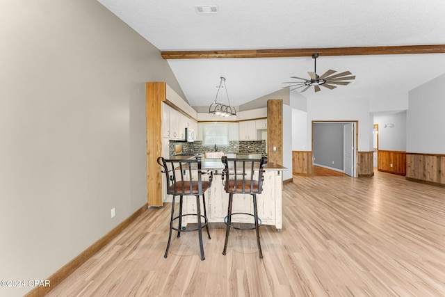 kitchen featuring vaulted ceiling with beams, kitchen peninsula, light hardwood / wood-style floors, decorative backsplash, and white cabinets