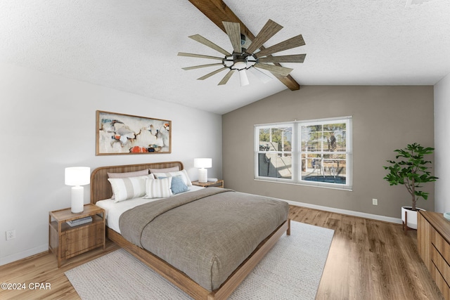 bedroom with ceiling fan, lofted ceiling with beams, wood-type flooring, and a textured ceiling