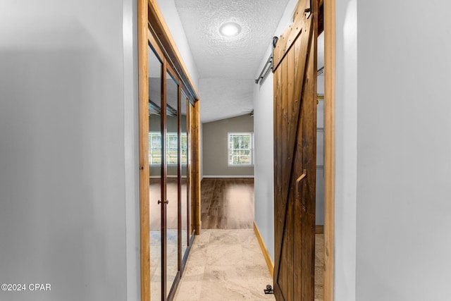 hall featuring a textured ceiling, a barn door, and lofted ceiling