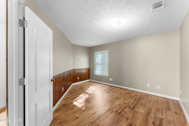 unfurnished room with wooden walls, light hardwood / wood-style floors, and a textured ceiling