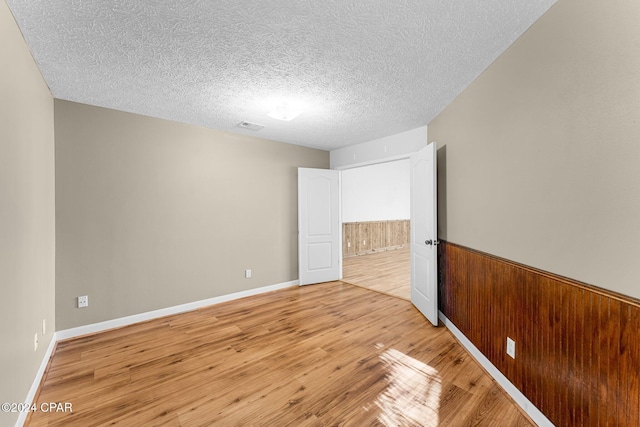 unfurnished bedroom with a textured ceiling, light hardwood / wood-style flooring, and wooden walls