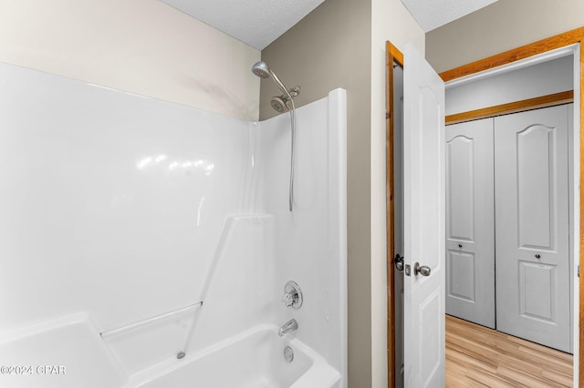 bathroom with hardwood / wood-style floors, a textured ceiling, and tub / shower combination