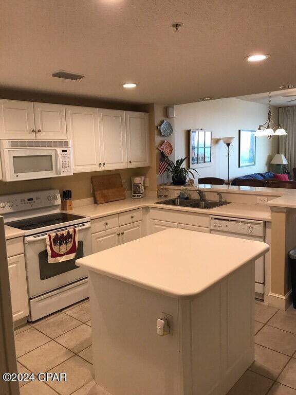 kitchen with white appliances, sink, light tile patterned floors, white cabinets, and a center island