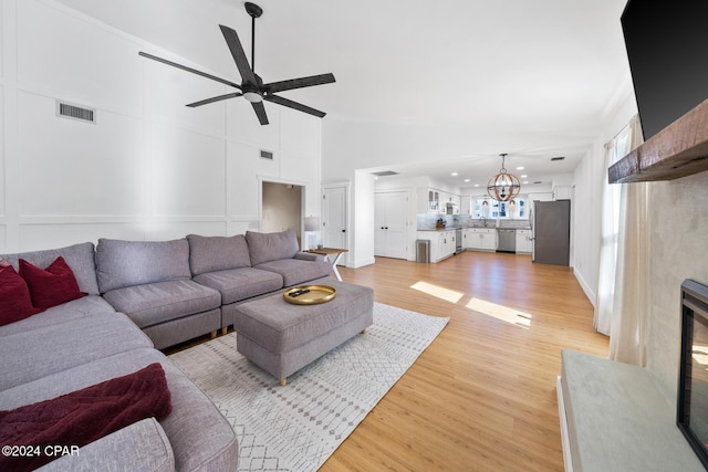 living room with ceiling fan with notable chandelier and light hardwood / wood-style floors