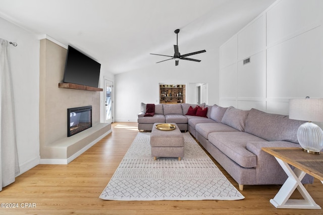 living room with ceiling fan, light hardwood / wood-style floors, and vaulted ceiling