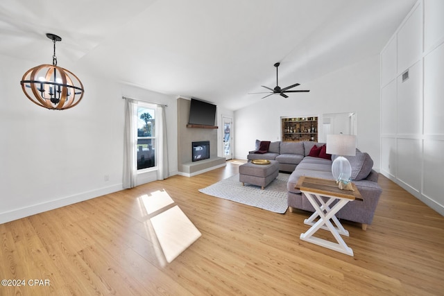 living room featuring a fireplace, light wood-type flooring, ceiling fan with notable chandelier, and lofted ceiling