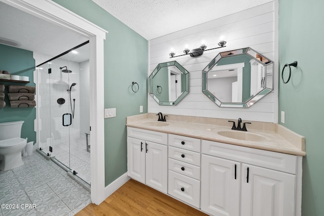 bathroom with vanity, hardwood / wood-style flooring, toilet, a textured ceiling, and a shower with shower door