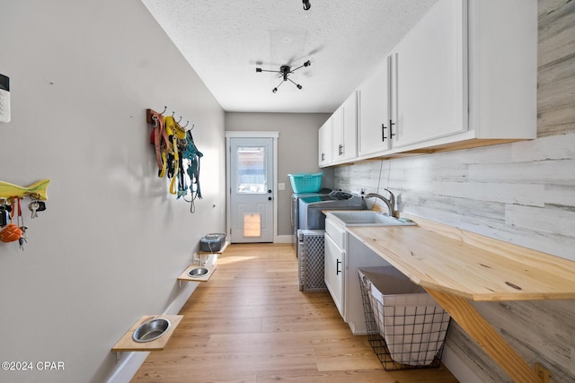 kitchen with white cabinets, sink, washer and dryer, a textured ceiling, and light hardwood / wood-style floors