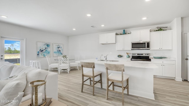 kitchen with a sink, light wood finished floors, appliances with stainless steel finishes, and white cabinetry