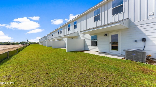 back of house with central air condition unit, board and batten siding, a yard, and fence