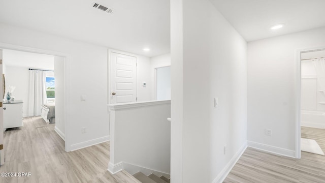 hall featuring baseboards, an upstairs landing, visible vents, and light wood finished floors