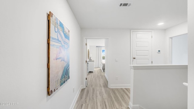 corridor featuring baseboards, visible vents, and light wood finished floors