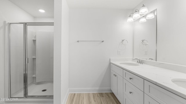 full bath with a shower stall, baseboards, double vanity, wood finished floors, and a sink