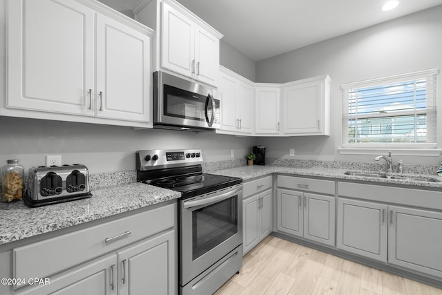 kitchen featuring stainless steel appliances, white cabinetry, a sink, and light stone countertops
