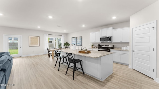 kitchen featuring a sink, light wood-type flooring, appliances with stainless steel finishes, and a center island with sink