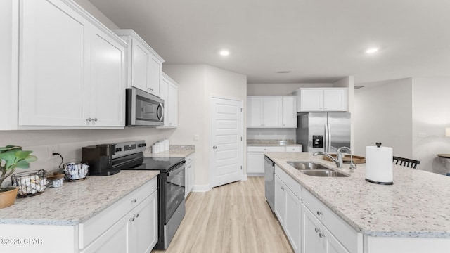 kitchen featuring a center island with sink, light wood-type flooring, stainless steel appliances, white cabinetry, and a sink