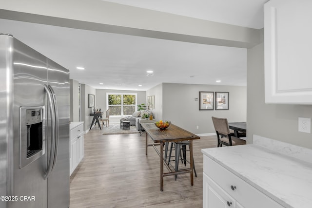 kitchen with white cabinetry, light wood-style flooring, light stone counters, and stainless steel fridge with ice dispenser