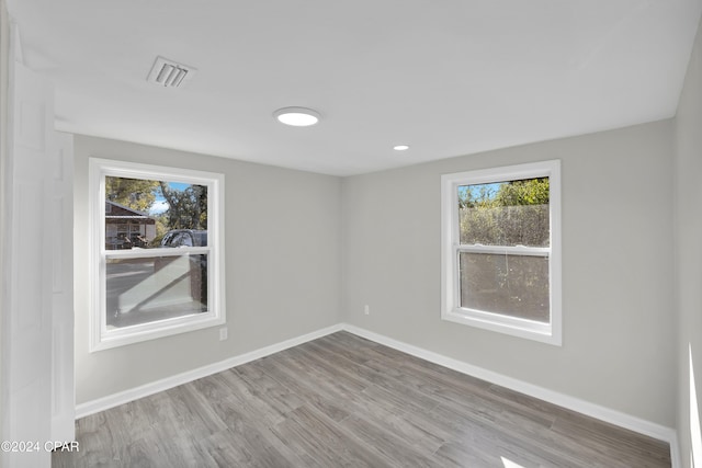 empty room featuring a wealth of natural light, visible vents, baseboards, and wood finished floors