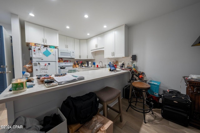 kitchen with kitchen peninsula, white appliances, white cabinets, and a breakfast bar