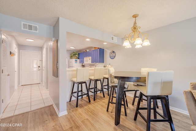 dining room with a notable chandelier, light hardwood / wood-style floors, and a textured ceiling