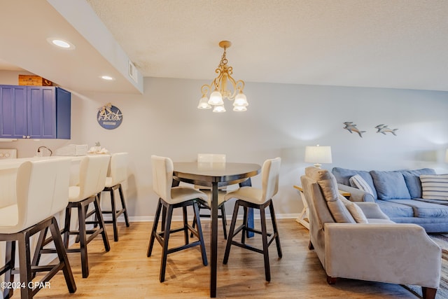 dining area with a textured ceiling, light hardwood / wood-style flooring, and an inviting chandelier