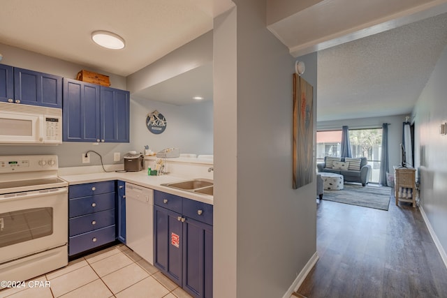 kitchen featuring blue cabinetry, white appliances, light tile patterned flooring, and sink