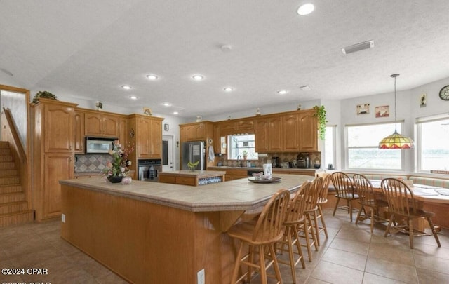 kitchen with pendant lighting, stainless steel appliances, a center island, tasteful backsplash, and light tile patterned flooring