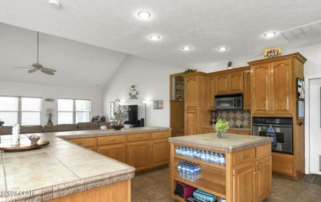 kitchen featuring tile countertops, vaulted ceiling, a kitchen island, oven, and decorative backsplash