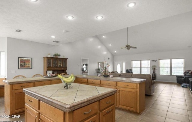 kitchen with ceiling fan, high vaulted ceiling, a center island, light tile patterned flooring, and tile countertops