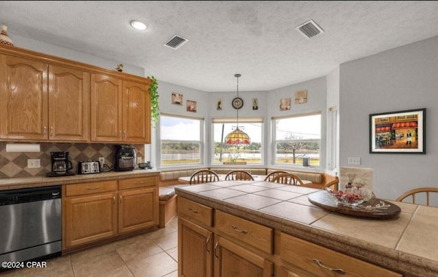 kitchen featuring tasteful backsplash, decorative light fixtures, a textured ceiling, stainless steel dishwasher, and tile counters