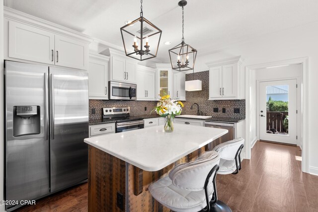 kitchen with a center island, white cabinets, sink, hanging light fixtures, and appliances with stainless steel finishes