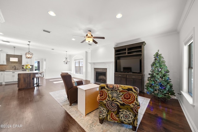 living room with hardwood / wood-style floors, ceiling fan with notable chandelier, ornamental molding, and sink