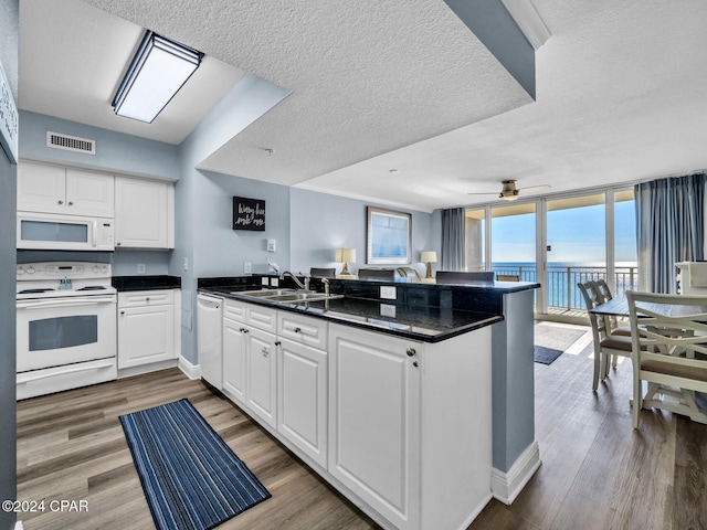 kitchen featuring a peninsula, white appliances, a sink, visible vents, and dark countertops