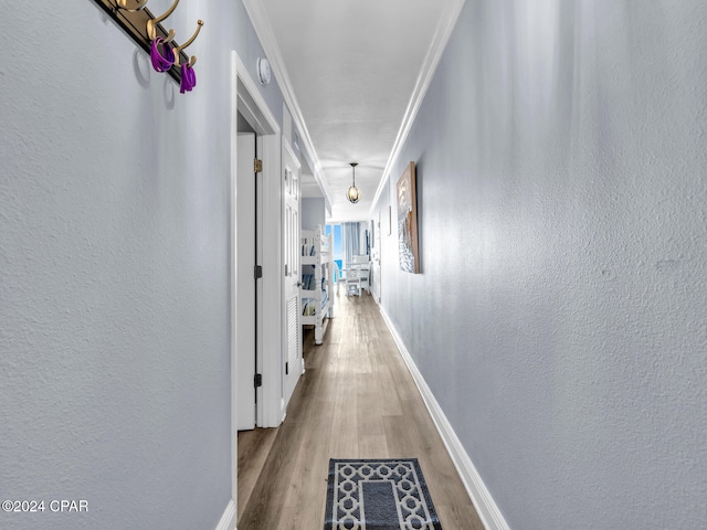 hallway with a textured wall, ornamental molding, wood finished floors, and baseboards