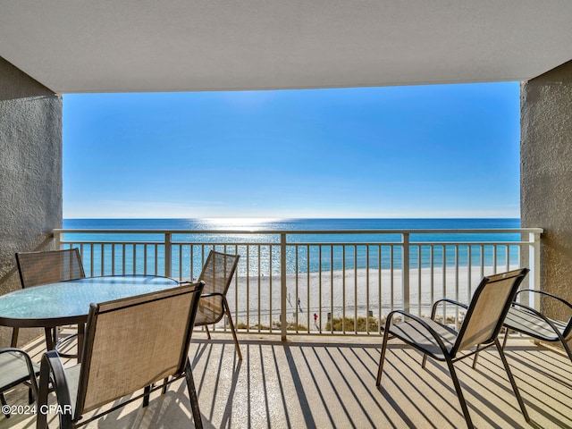 balcony featuring a view of the beach, outdoor dining space, and a water view