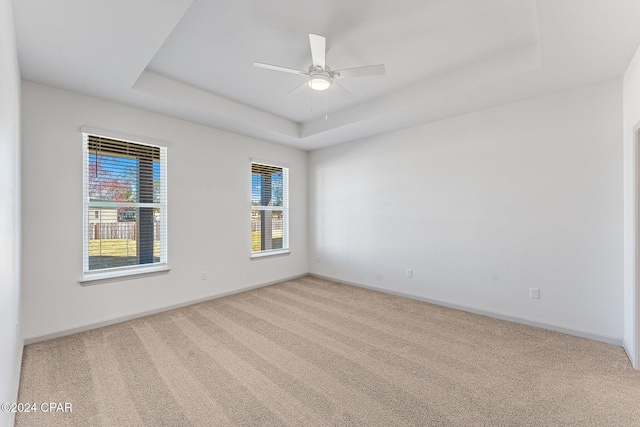 carpeted spare room featuring ceiling fan, baseboards, and a tray ceiling