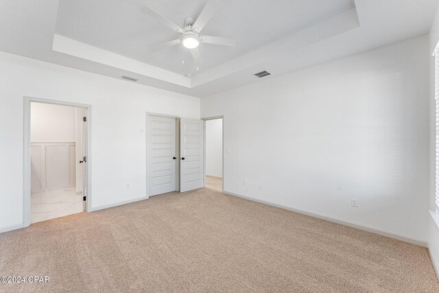 unfurnished bedroom with light carpet, visible vents, a raised ceiling, and baseboards