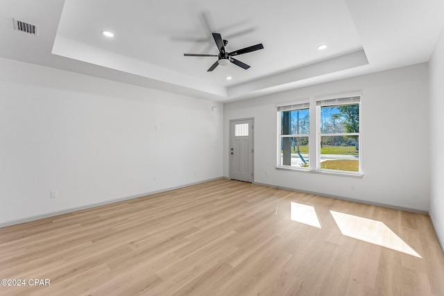 empty room with a tray ceiling, light wood-style floors, visible vents, and ceiling fan