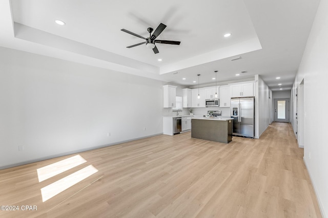 kitchen featuring a tray ceiling, a kitchen island, open floor plan, white cabinetry, and appliances with stainless steel finishes