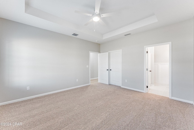 unfurnished bedroom with visible vents, baseboards, ensuite bathroom, a raised ceiling, and light colored carpet