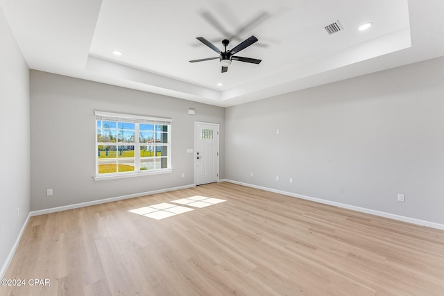 spare room with a tray ceiling, visible vents, baseboards, and light wood-style flooring