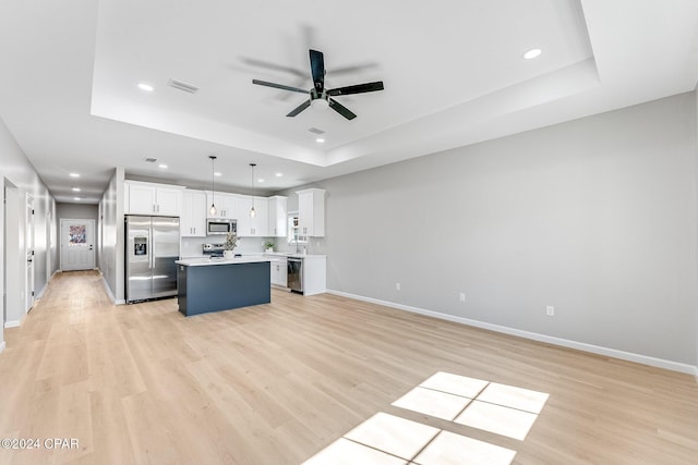 kitchen featuring a ceiling fan, a tray ceiling, a center island, white cabinetry, and appliances with stainless steel finishes