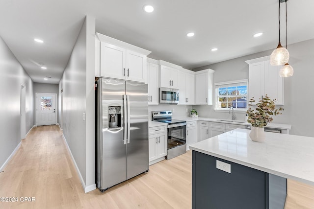 kitchen with a sink, stainless steel appliances, white cabinets, pendant lighting, and light wood-type flooring