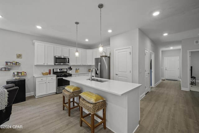 kitchen with a kitchen bar, stainless steel appliances, sink, pendant lighting, and white cabinetry