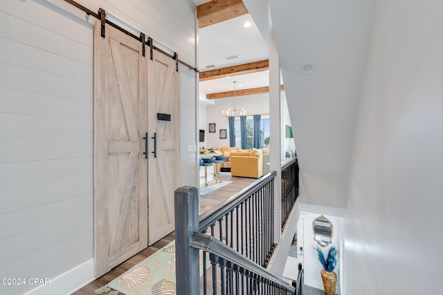 hall featuring a barn door, hardwood / wood-style flooring, a notable chandelier, beamed ceiling, and wood walls