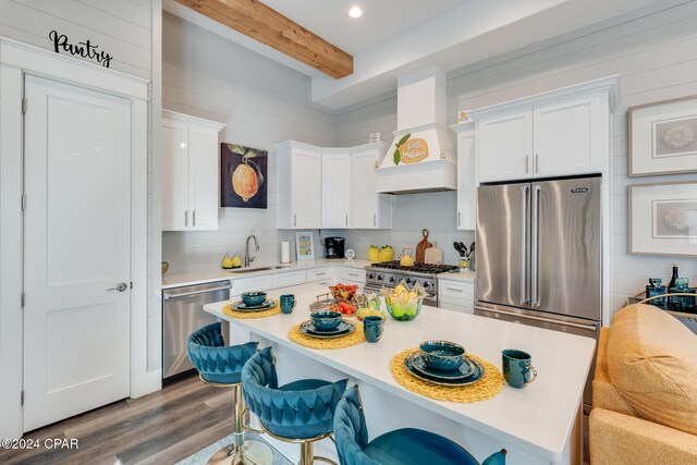 kitchen featuring premium range hood, white cabinets, a kitchen breakfast bar, premium appliances, and beam ceiling