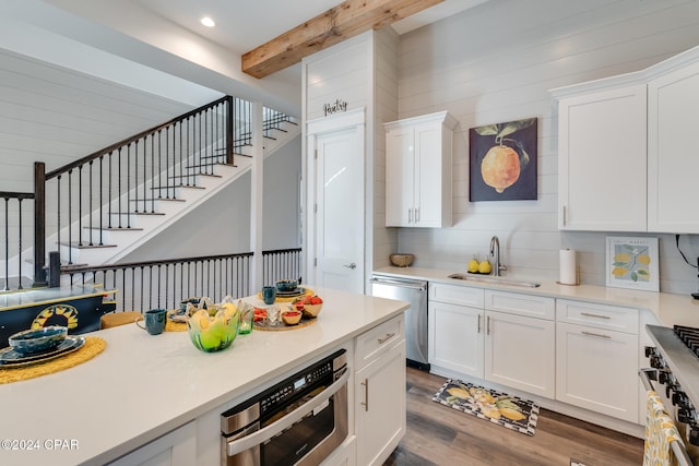 kitchen with appliances with stainless steel finishes, white cabinets, dark wood-type flooring, sink, and beamed ceiling